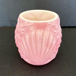 Puede incluir: Una taza de cerámica rosa con un diseño de concha. La taza tiene un acabado liso y brillante y un exterior rosa claro con un interior blanco. El diseño de concha está en relieve en el exterior de la taza.
