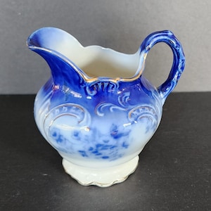 May include: A small blue and white porcelain creamer with a delicate floral design and gold accents. The creamer has a rounded body and a small spout.
