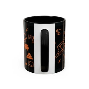 May include: Black ceramic mug with a white vertical stripe and a black handle. The mug is decorated with orange geometric shapes and symbols, including lightning bolts, squares, and a hand.