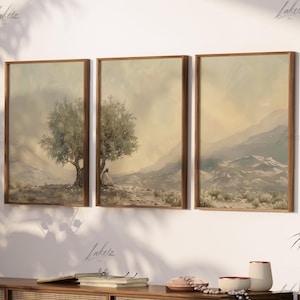 May include: Three framed landscape paintings with a muted color palette. The paintings depict a lone tree in a desert landscape, with mountains in the background. The frames are a light brown wood.