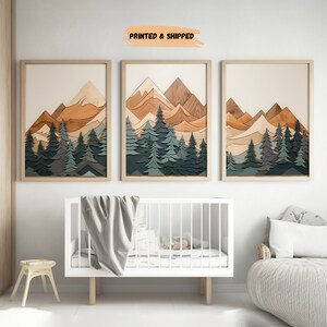 May include: Three framed prints of a mountain landscape with a layered wood effect. The mountains are in shades of brown and orange, and the trees are in shades of green and blue. The prints are arranged in a row on a white wall.