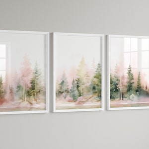 Op de afbeelding: Een set van drie ingelijste aquarellen die een bos sc&egrave;ne afbeelden in roze en groene tinten. De schilderijen zijn in witte lijsten en hangen aan een witte muur.