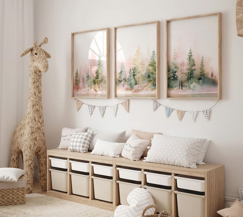 Op de afbeelding: Een lichte houten opbergbank met witte bakken en een geweven giraffenknuffel. Boven de bank hangen drie ingelijste aquarelprints van een boslandschap met een string van kleurrijke vlaggetjes.