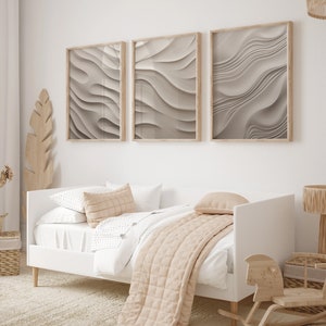 May include: A white daybed with a beige blanket and pillows, set against a white wall with three framed abstract prints of wavy lines in shades of gray.