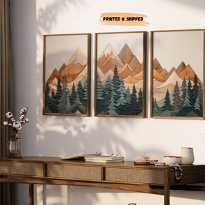 May include: Three framed prints of a layered wood art piece depicting a mountain range with a forest in the foreground. The mountains are in shades of brown, orange, and beige, while the trees are in shades of green and blue. The text "PRINTED & SHIPPED" is visible at the top of the image.