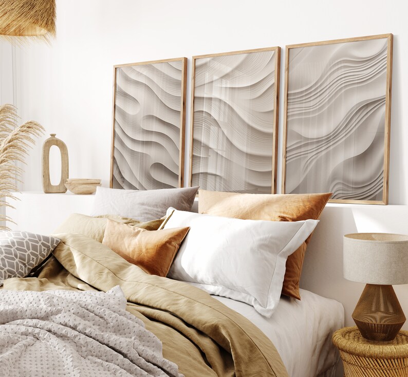 May include: A bedroom with a bed made with a brown duvet and white and brown pillows. Three framed abstract prints with a wavy pattern in shades of beige and white hang above the bed.