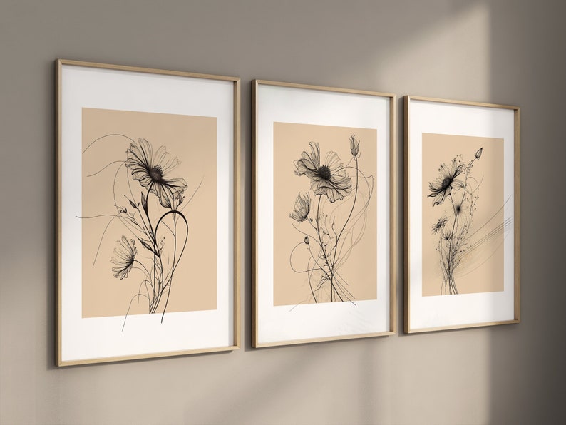 以下が含まれることがあります： ベージュの背景に黒い線で描かれた花が描かれた額装されたプリントが3枚。花はスタイリッシュで、繊細で軽やかな印象です。