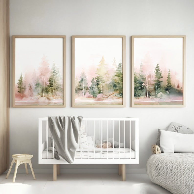 Op de afbeelding: Drie ingelijste aquarellen van een boslandschap in roze en groene tinten. De schilderijen hangen aan een witte muur boven een wit babybedje.