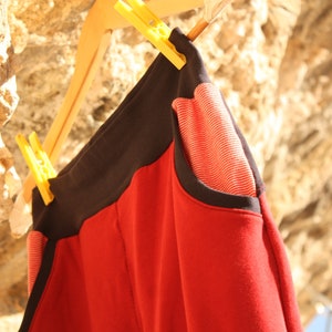 May include: Red and black sweatpants with a striped pocket detail hanging on a wooden hanger.