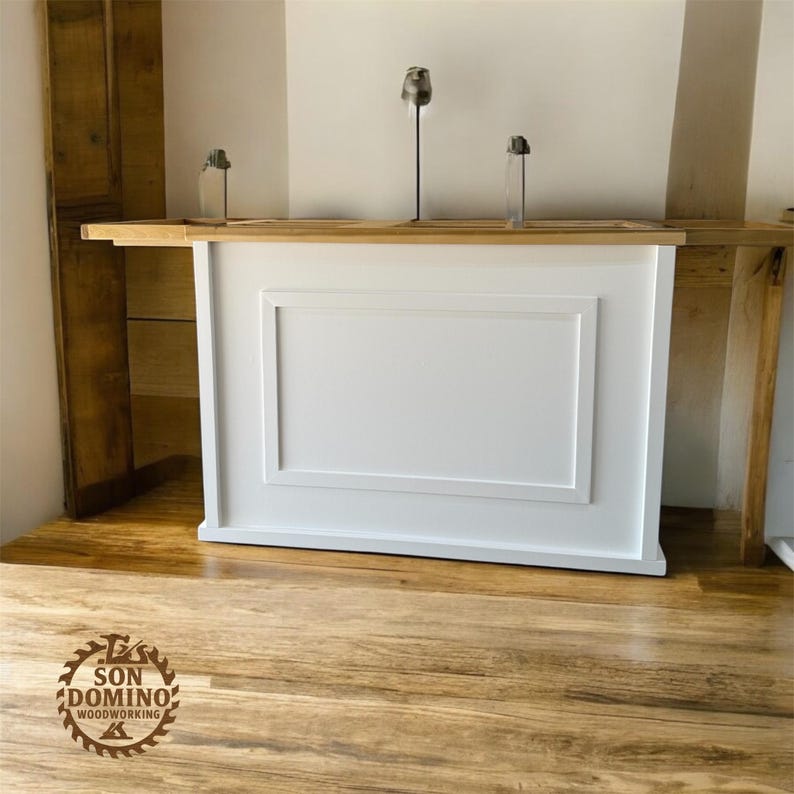 May include: A white wooden bar with a rectangular panel design. The bar is set against a light-coloured wall and a wooden shelf. The floor is made of wood. The logo "SON DOMINO WOODWORKING" is visible on the floor.