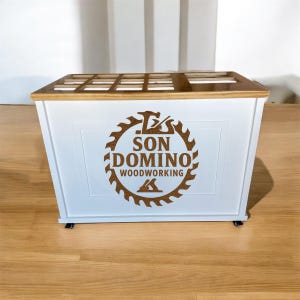 May include: A white wooden box with a brown wooden top and the text "SON DOMINO WOODWORKING" in a circular design. The box is rectangular and may be used for storage or display.