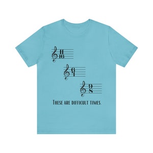 Peut inclure: Un t-shirt bleu clair avec un motif de notes de musique et le texte "These are difficult times."