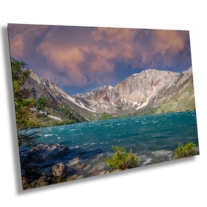 May include: A scenic view of a mountain lake with a dramatic sky. The lake is a vibrant turquoise blue and the mountains are a mix of green, brown, and white. The sky is a deep blue with pink and orange clouds.