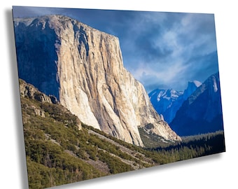 Könnte beinhalten: Ein Panoramablick auf eine hoch aufragende Felsformation im Yosemite-Nationalpark. Die Felswand ist hellbeige und von üppigem Grün umgeben. Der Himmel ist strahlend blau mit weißen Wolken.