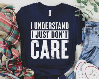 May include: A navy blue t-shirt with white text that reads "I understand I just don't care". The shirt is laid out on a white surface with a plaid blanket and blue jeans.
