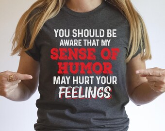 May include: A dark gray t-shirt with white text that reads "You should be aware that my sense of humor may hurt your feelings". The text "sense of humor" is in red.