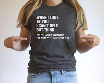 May include: A dark gray t-shirt with white text that reads "WHEN I LOOK AT YOU I CAN'T HELP BUT THINK 'WHY HASN'T SOMEONE HIT YOU WITH A SHOVEL YET?"