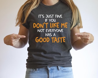May include: A dark gray t-shirt with the text "It's just fine if you don't like me not everyone has a good taste" in white with the words "don't like me" and "good taste" in orange.