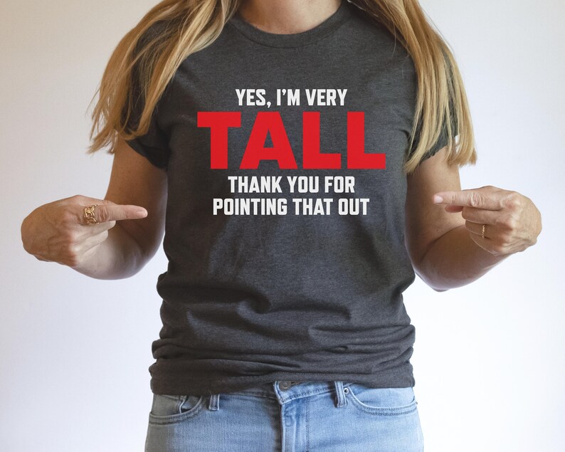 Puede incluir: Una camiseta gris oscuro con el texto "YES, I'M VERY TALL THANK YOU FOR POINTING THAT OUT" en letras blancas. La palabra "TALL" est&aacute; en rojo.