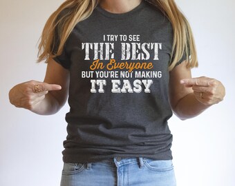 May include: A dark gray t-shirt with the text "I try to see the best in everyone but you're not making it easy". The text is in white with the words "best" and "everyone" in orange.