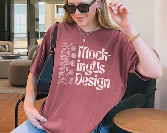 May include: A maroon t-shirt with the text "MockingUs Design" in white, and floral illustrations. The shirt is worn with blue jeans and a black headband. The person is wearing sunglasses and gold jewellery.