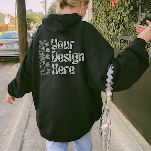Back view of a real model wearing an oversized Black Gildan 18500 hooded sweatshirt in a moody outdoor streetwear setting.