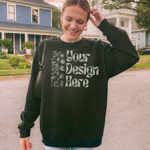 Black Gildan 18000 sweatshirt mockup. Model is showing front of the oversized crewneck. It is an outdoor lifestyle photo with a trendy Y2K aesthetic.