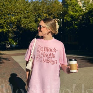 Female model on the sidewalk in the city wearing an oversized blossom C1717 Comfort Colors t-shirt. Image shows the front of shirt. Woman is wearing trendy accessories for a streetwear aesthetic.