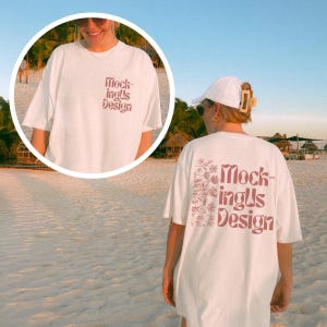 May include: White oversized t-shirt with the text "MockingUs Design" in reddish-brown on the front and back. The back of the shirt also features a floral design in the same colour. The shirt is worn on a beach.