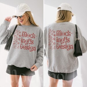 Puede incluir: Una sudadera gris jaspeada con el texto "MockingUs Design" en marrón rojizo. El diseño está en la parte delantera y trasera de la sudadera. La sudadera se combina con una falda negra y un bolso negro.