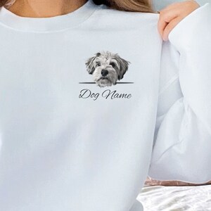 May include: White sweatshirt with a graphic of a dog's head peeking over a line with the text "Dog Name" underneath.