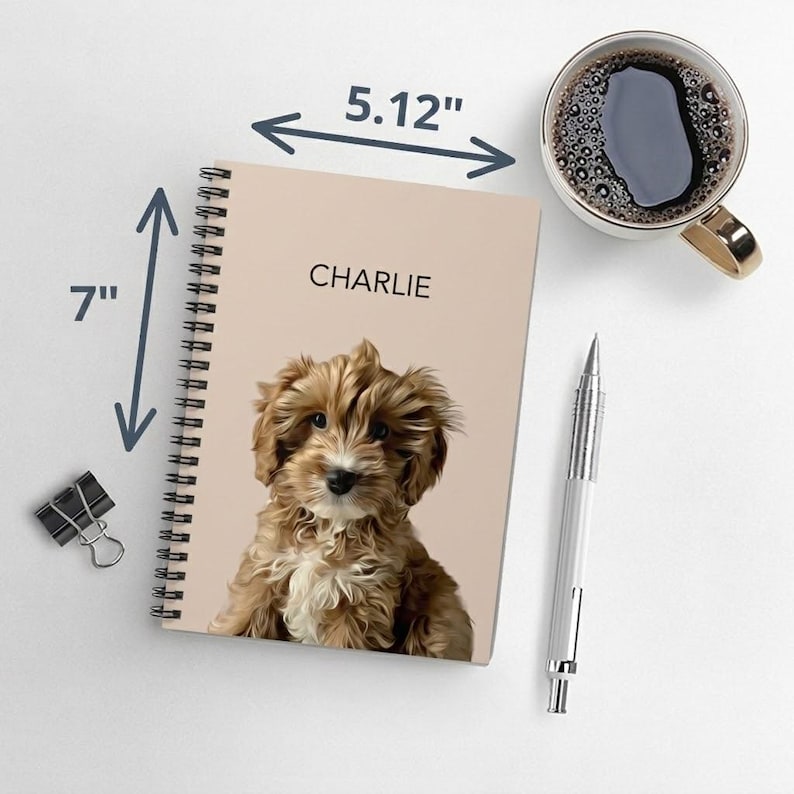 May include: A spiral-bound notebook with a light beige cover featuring a digital illustration of a brown and white puppy and the name CHARLIE printed in black. The notebook measures 5.12 inches in width and 7 inches in height.