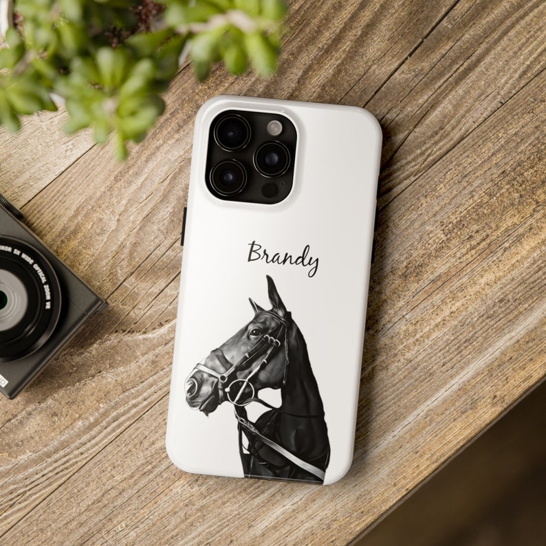 May include: White iPhone case featuring a black and white illustration of a horse's head. The name "Brandy" is printed in black at the top of the case.