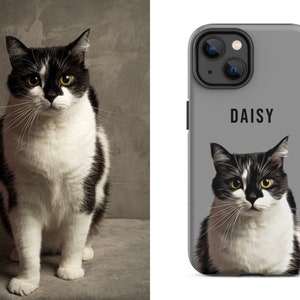 May include: A black and white cat with yellow eyes sits next to a gray phone case. The phone case features a portrait of the cat with the name "DAISY" printed above the image. The cat has a white chest and paws.