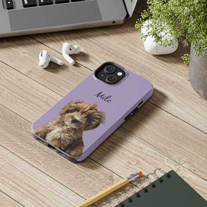May include: A lavender phone case featuring a brown and white puppy with the name "Milo" in script. The case is on a wooden surface with a laptop, earbuds, and a pencil.