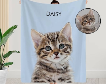 May include: A light blue fleece blanket with a personalized image of a tabby cat with green eyes. The cat's name, "DAISY", is printed in black text above the image.