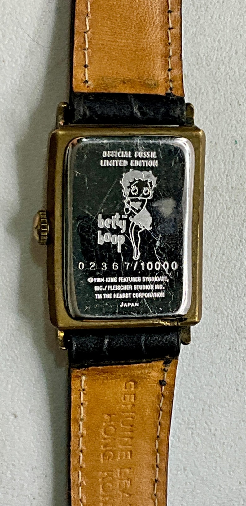Peut inclure: Montre officielle Fossil en &eacute;dition limit&eacute;e avec Betty Boop. La montre a un bo&icirc;tier rectangulaire dor&eacute; avec un bracelet en cuir noir. Le cadran affiche le logo Betty Boop et le texte "0236 7/10000".