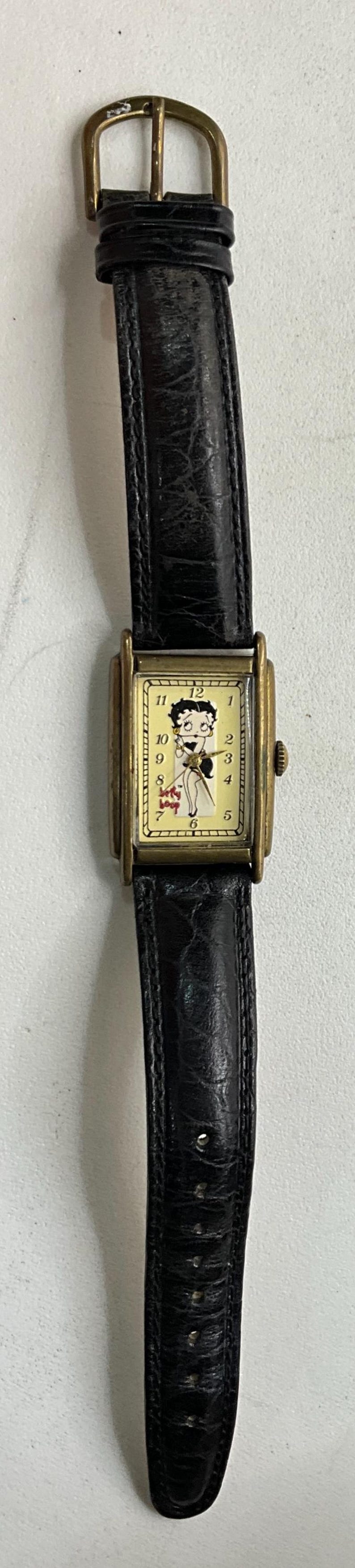 Peut inclure: Montre-bracelet vintage Betty Boop avec un bracelet en cuir noir et un bo&icirc;tier dor&eacute;. Le cadran de la montre pr&eacute;sente un graphisme Betty Boop et un fond cr&egrave;me. Une montre classique.