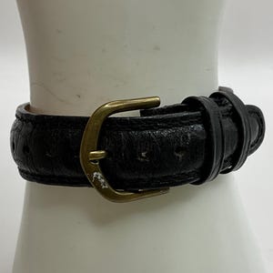 Peut inclure: Gros plan sur un bracelet de montre en cuir noir avec une boucle dor&eacute;e. Le bracelet est textur&eacute; et semble us&eacute;. La boucle est de conception classique.