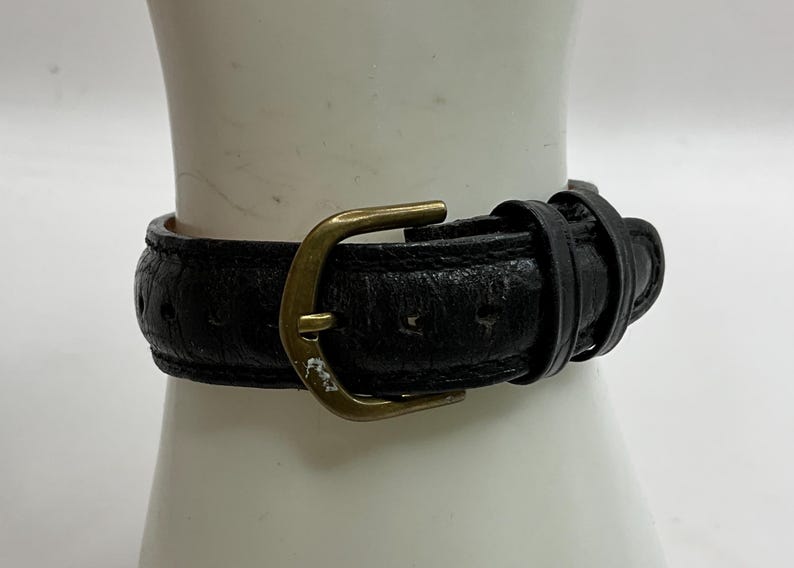 Peut inclure: Gros plan sur un bracelet de montre en cuir noir avec une boucle dor&eacute;e. Le bracelet est textur&eacute; et semble us&eacute;. La boucle est de conception classique.