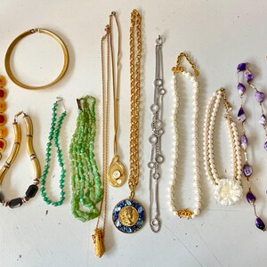May include: A selection of vintage necklaces and bracelets. The jewellery includes gold and silver chains, beaded strands, and statement pieces with red, green, and purple accents. A gold collar necklace and a bracelet with red stones are also visible.