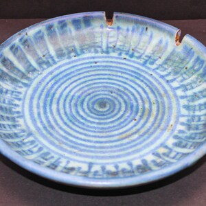 May include: A blue and white ceramic bowl with a spiral pattern. The bowl has a slightly raised rim and a small indentation on the side.