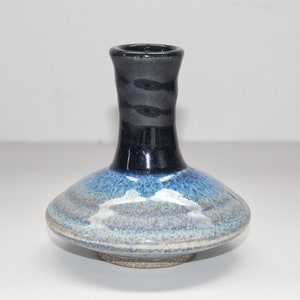 May include: A small, blue and black ceramic vase with a wide base and a narrow neck. The vase has a mottled glaze with shades of blue and white.