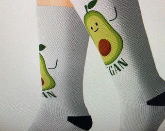May include: A pair of white socks with a green avocado graphic and the word "vegan" on one sock. The avocado has a smiling face and arms.