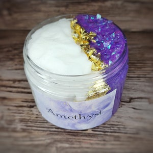 Könnte beinhalten: Ein klares Glas gefüllt mit lila und weißem Schleim mit goldenen Flocken. Das Glas hat ein Etikett mit der Aufschrift "Amethyst" und der Text "SLIMESALL" ist unter dem Glas sichtbar.