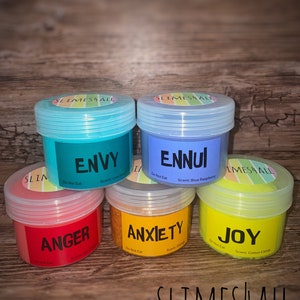 Könnte beinhalten: Sechs kleine Gläser mit Schleim, jedes mit einer anderen Farbe und einem anderen Duft. Die Gläser sind mit den Worten "Envy", "Ennui", "Anger", "Anxiety", "Joy" und "Slime 4 All" beschriftet.