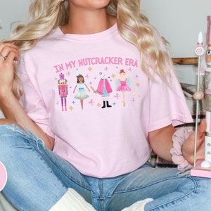 May include: Pink t-shirt with the text "In My Nutcracker Era" and a graphic of a nutcracker, a ballerina, and a mouse.