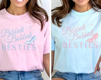 Pode incluir: Duas mulheres vestindo camisetas rosa e azul claro com o texto "Bibbidi Bobbidi Besties" e um gráfico de sapato de vidro.