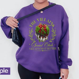 May include: A purple sweatshirt with a graphic design featuring a green skull with a red bow, surrounded by a laurel wreath. The text reads "The Villains Social Club, Villains Do It Better."