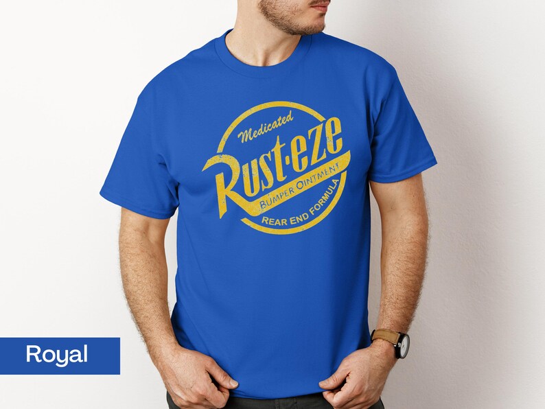 May include: Royal blue t-shirt featuring a yellow and gold circular graphic with the text "Medicated Rust-eze Bumper Ointment Rear End Formula". The shirt is a short-sleeved crew neck.